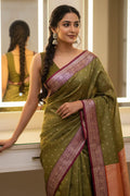 Woman wearing a green saree with a pink border in a well-lit room.