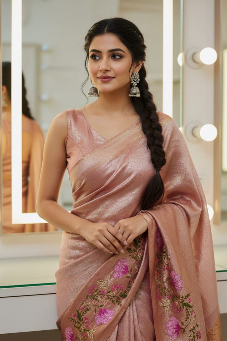 Woman in a pink saree with floral patterns standing in front of a mirror.