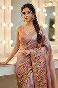 Woman wearing a pink saree with floral patterns in a well-lit room.