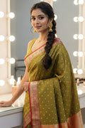 Woman in a green saree with a braid standing in front of a mirror with lights.