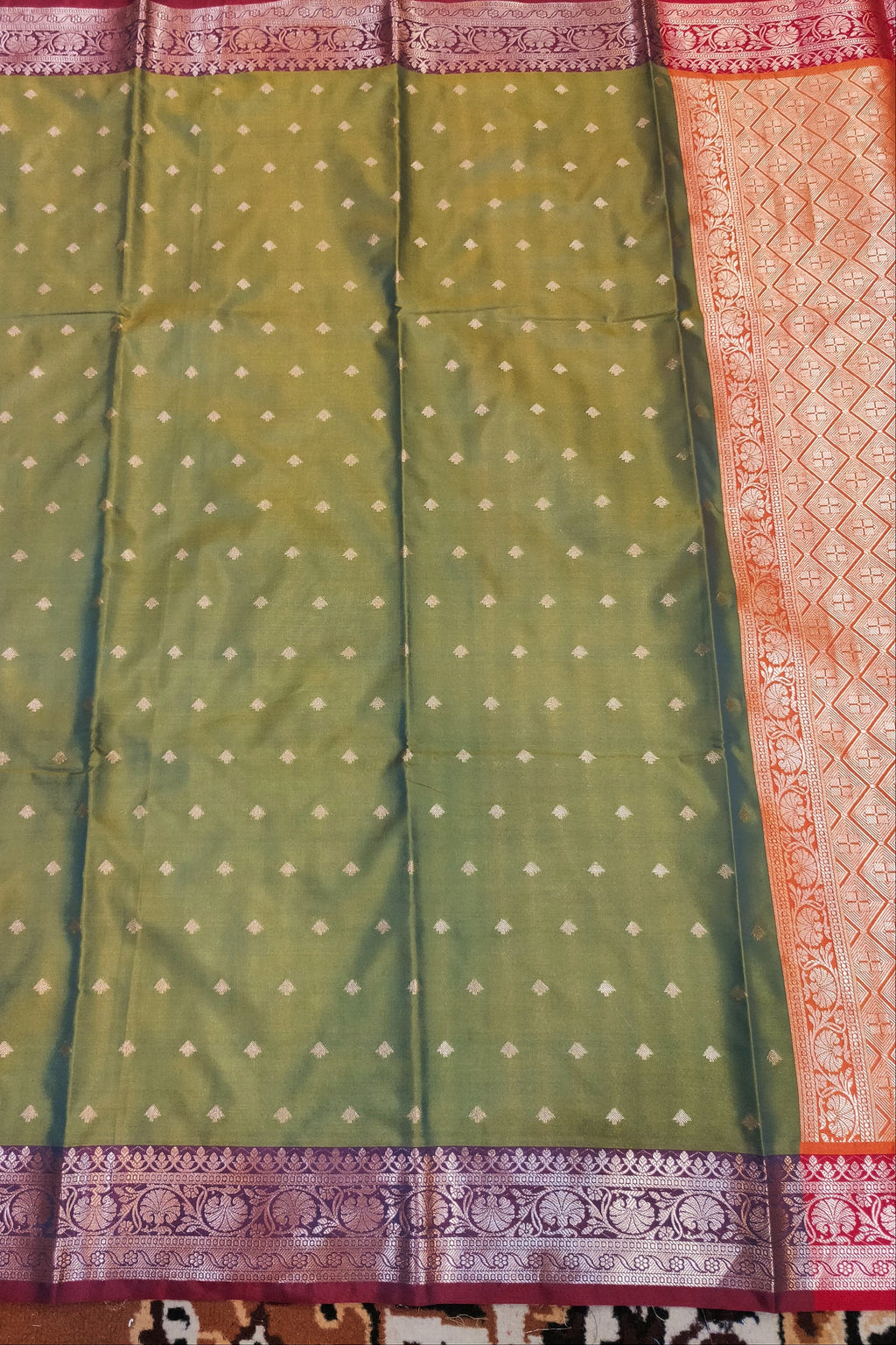 Green saree with white patterns and a red border on a patterned fabric background