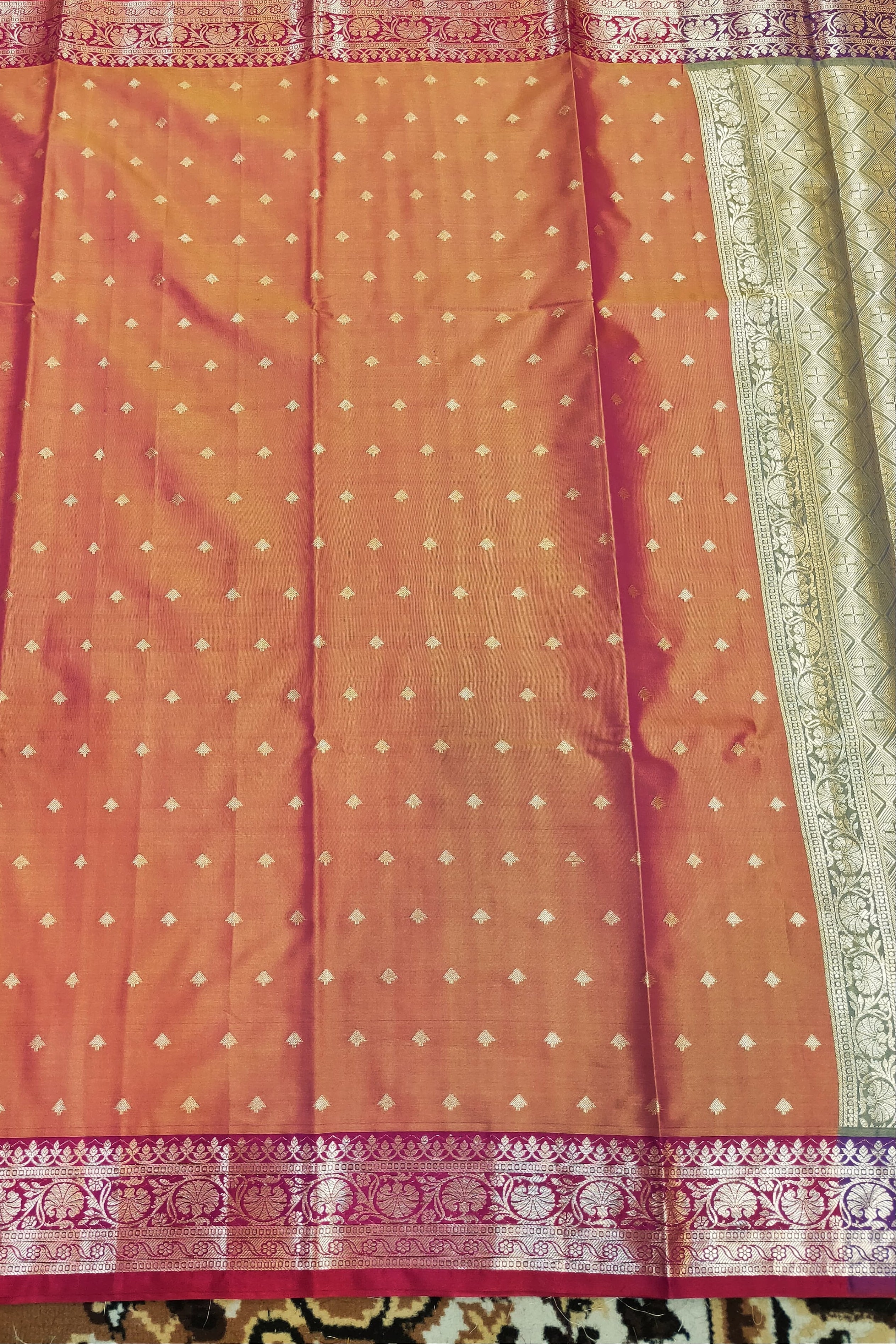 Orange saree with white patterns and pink border on a patterned fabric background