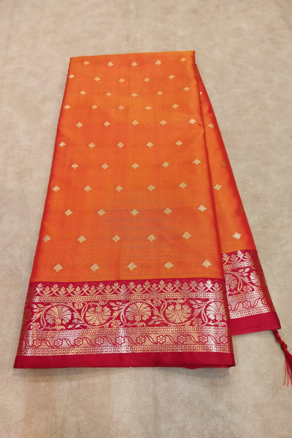 Orange and red saree with gold patterns on a beige background