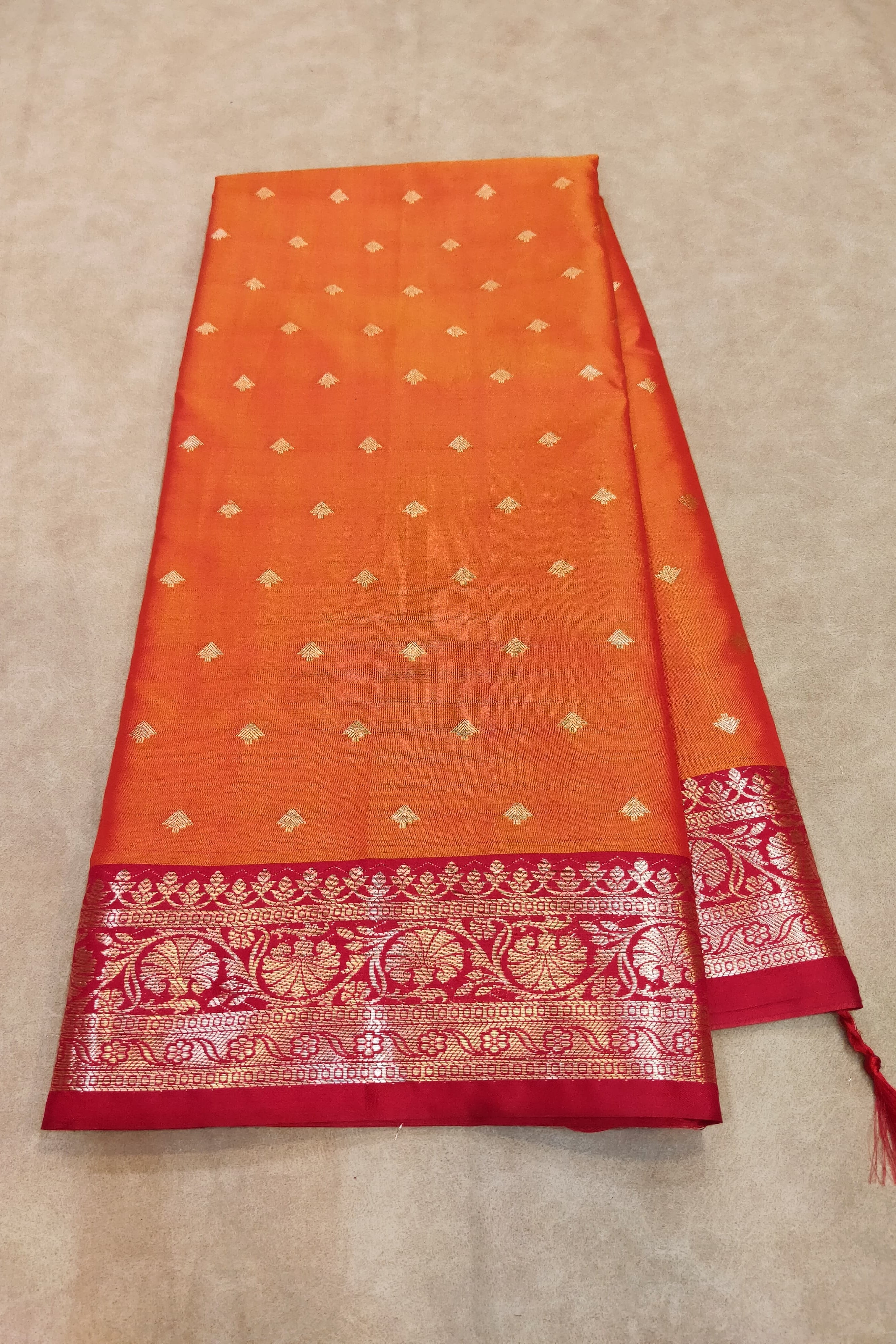 Orange and red saree with gold patterns on a beige background