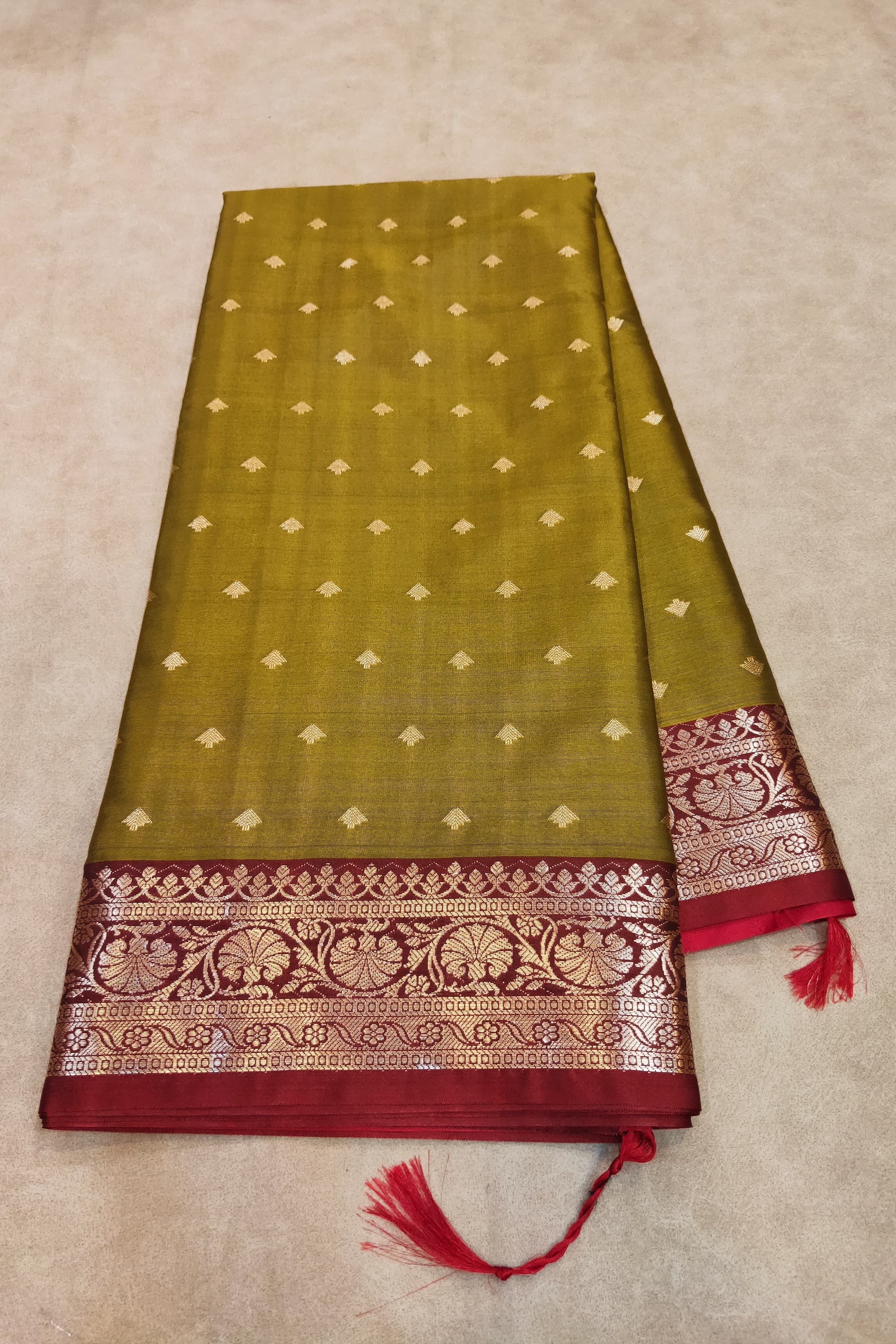 Green saree with red border and tassels on a beige background