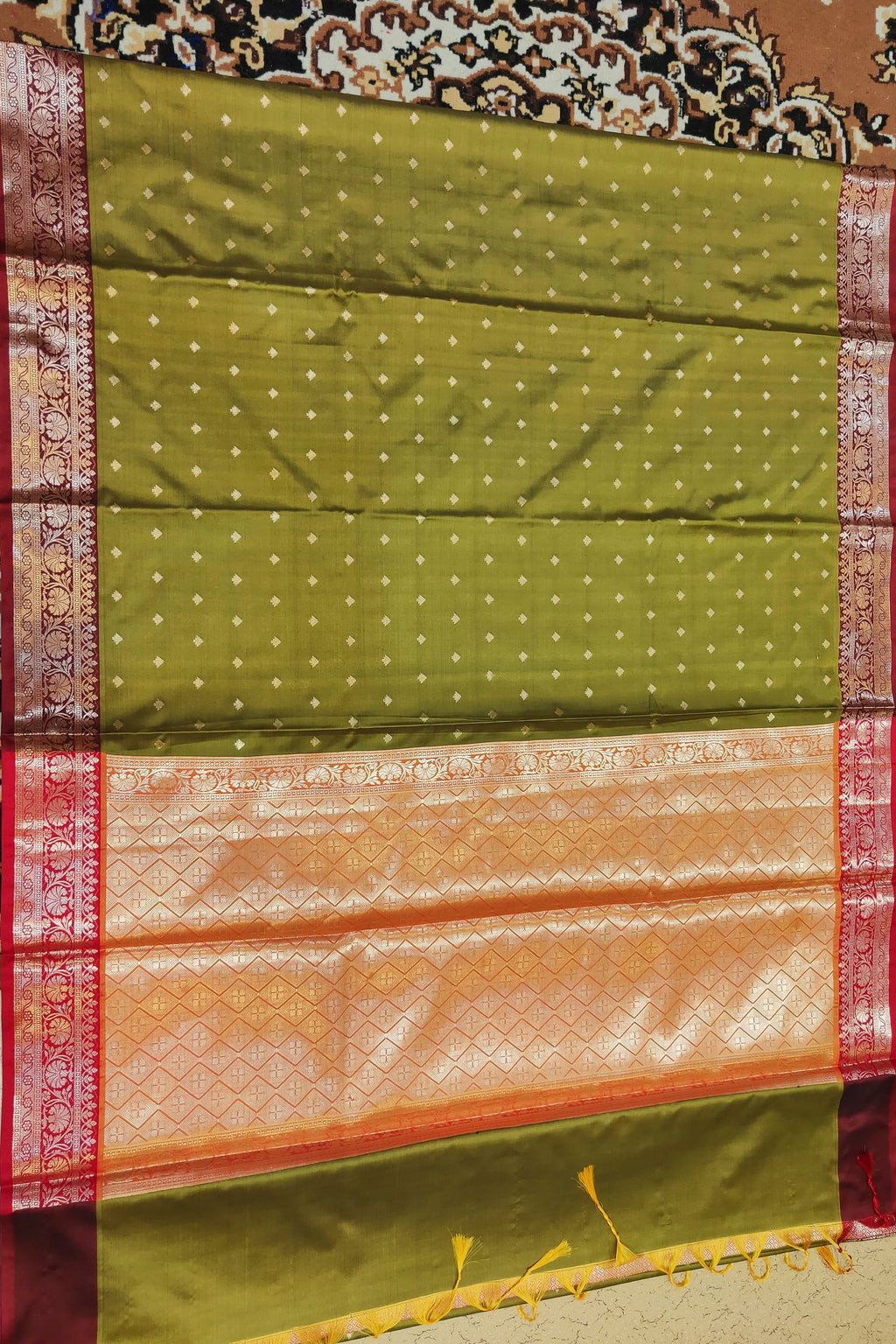 Green and orange saree with red border on a patterned fabric background