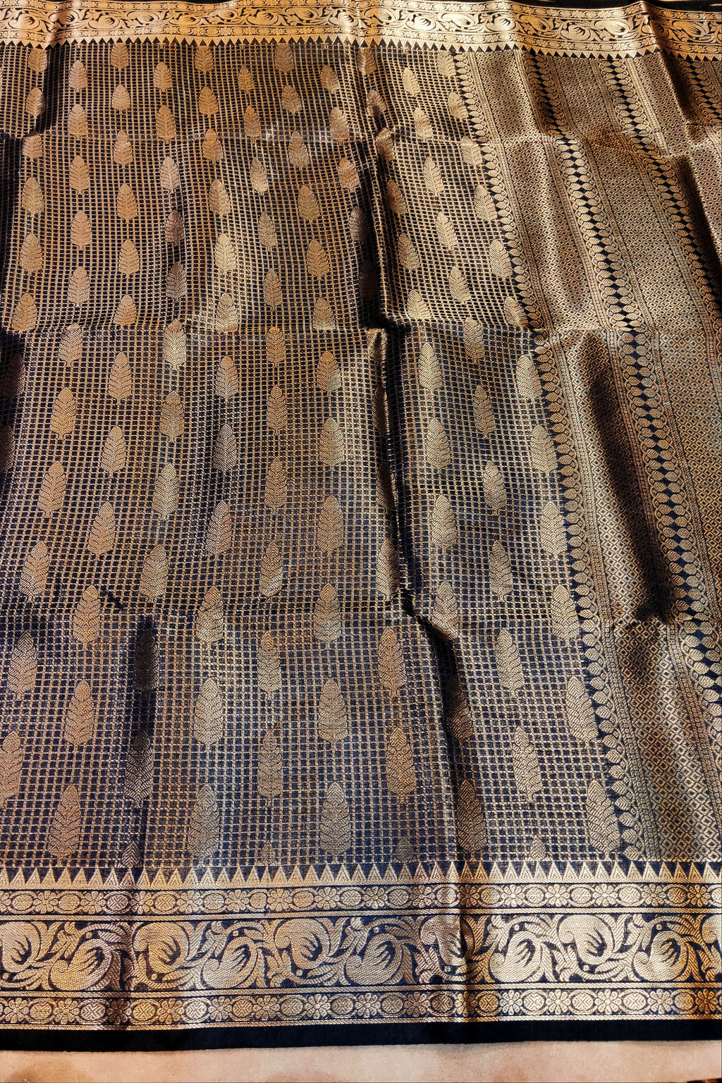 Black saree with gold patterns on a wooden surface