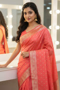 Woman in a coral saree with gold patterns standing in front of a mirror.