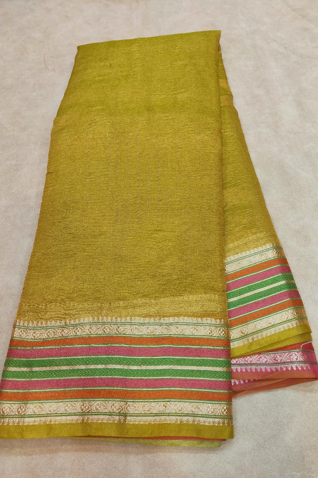 Green fabric with colorful striped border on a beige background