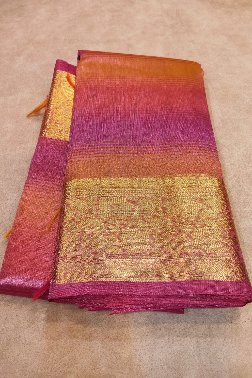 Folded fabric with red and gold pattern on a beige surface