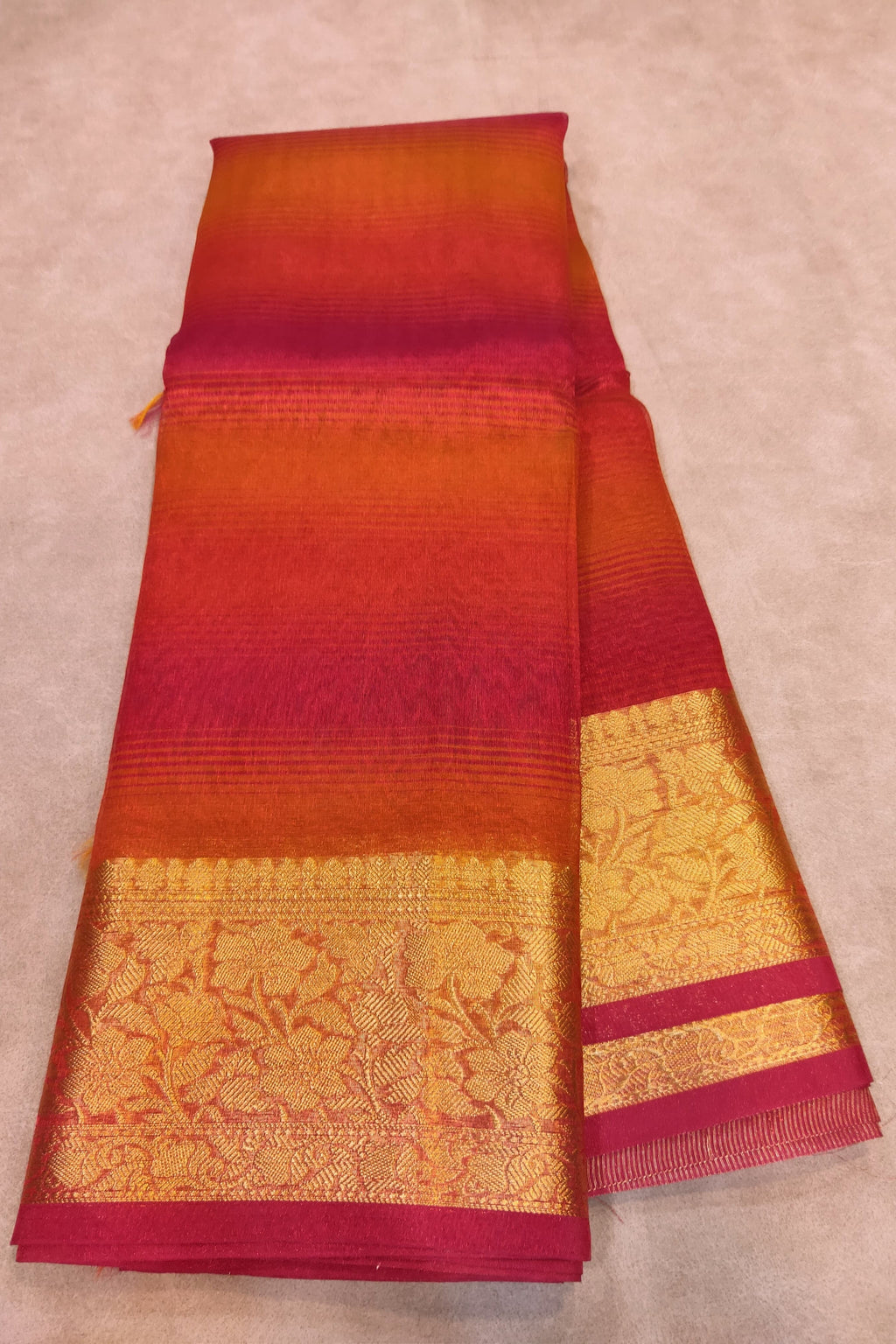 Red and orange saree with gold border on a beige background
