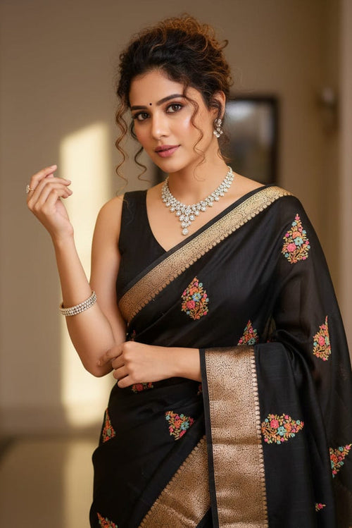 Woman wearing a black saree with gold and floral patterns indoors.