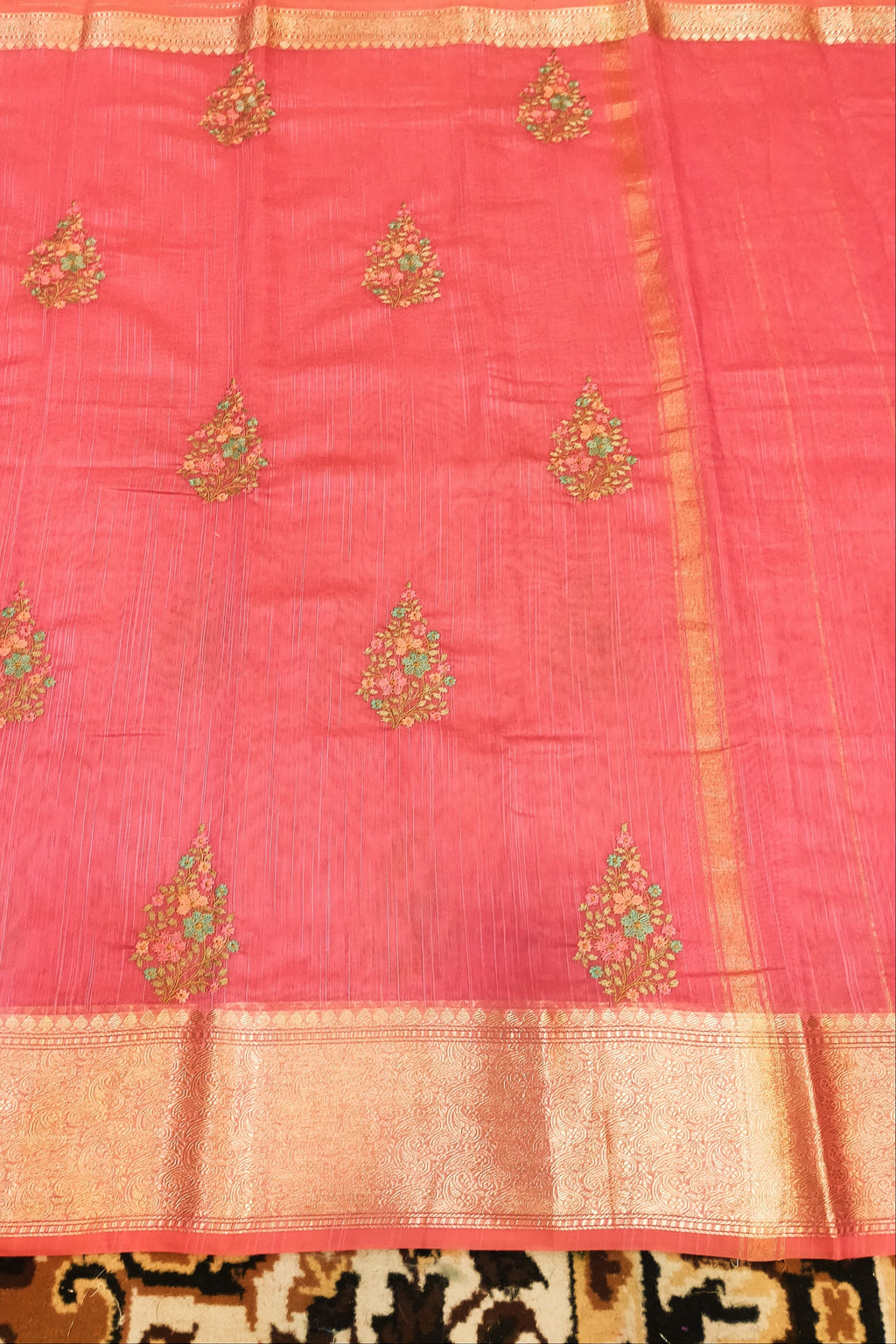 Pink saree with gold and green embroidery on a patterned fabric background