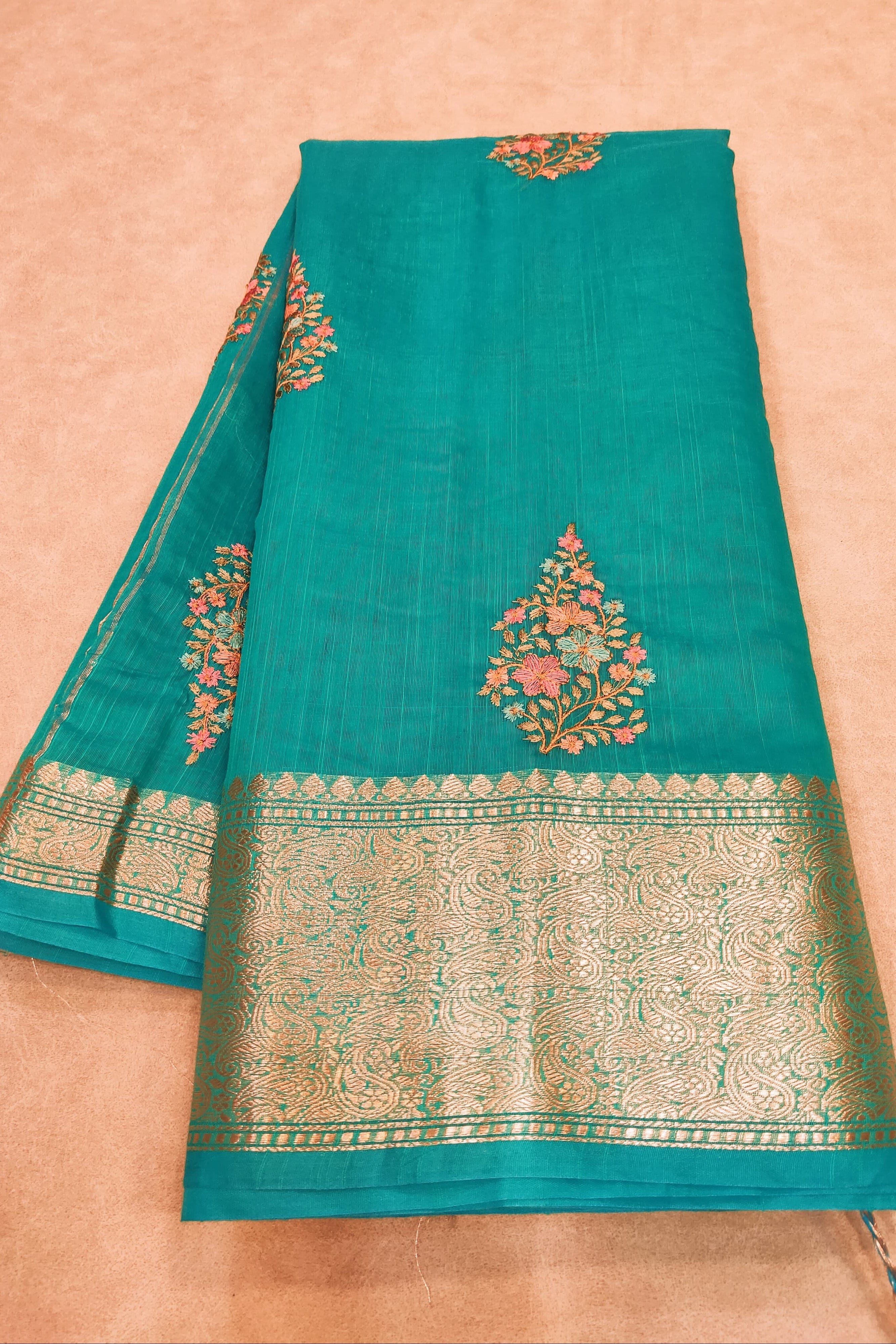 Teal fabric with gold and red embroidery on a beige background