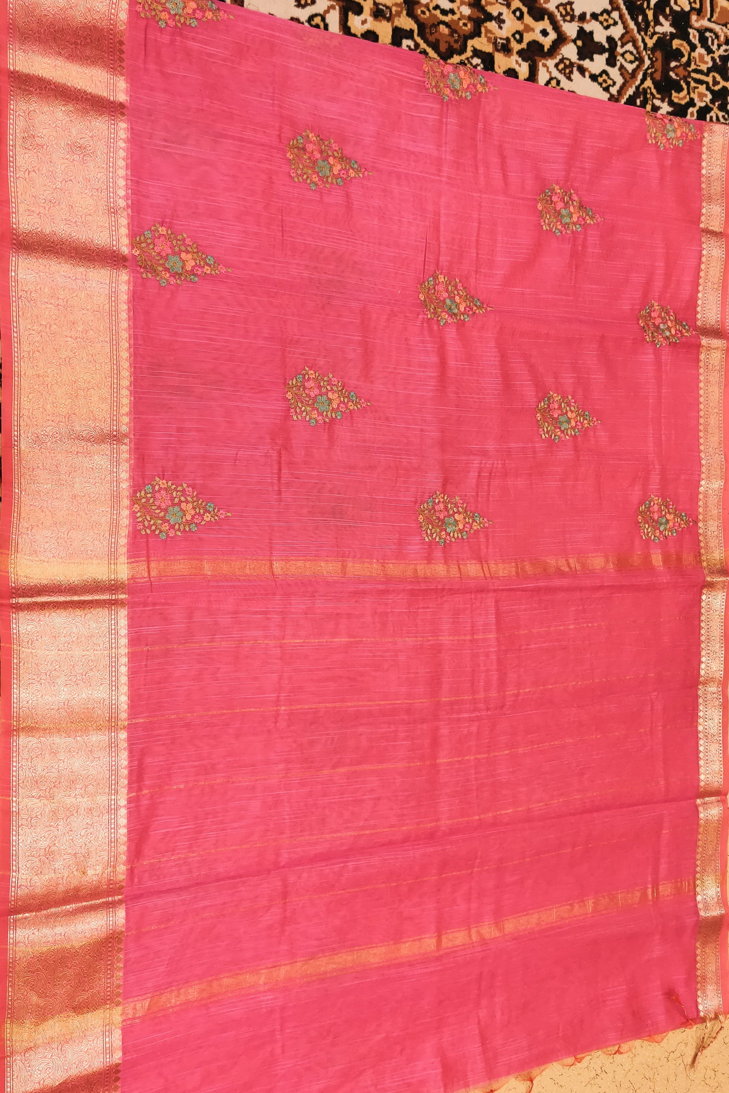 Pink saree with gold border and floral patterns on a patterned background