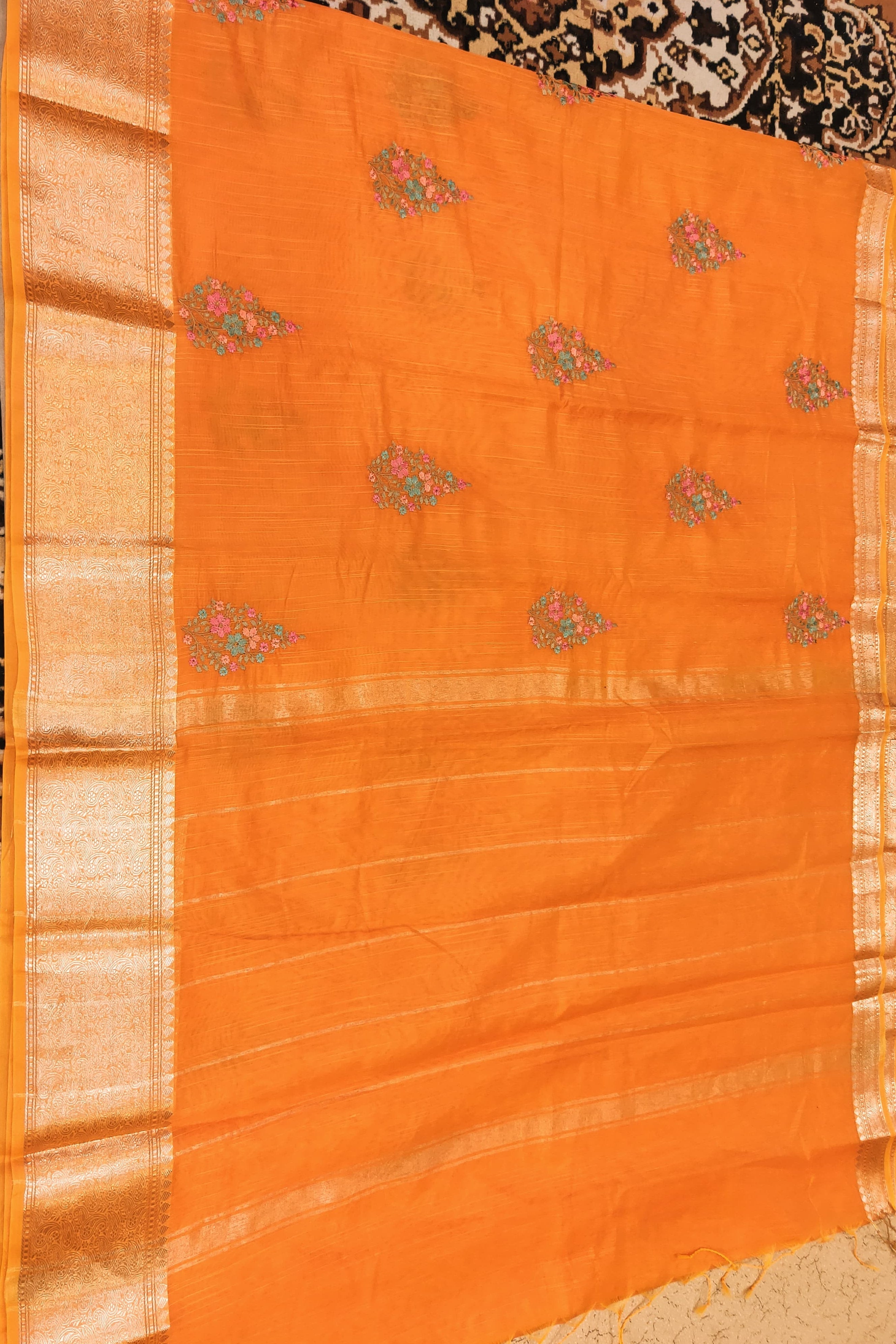 Orange saree with gold border and floral patterns on a textured surface