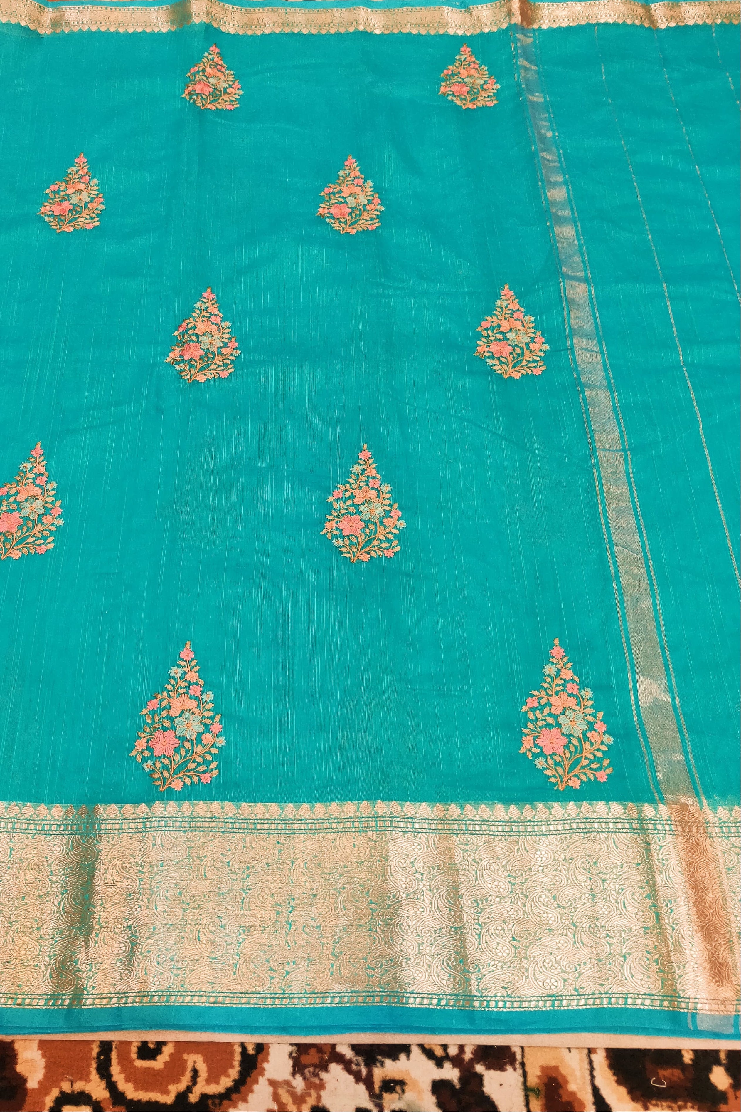 Turquoise saree with gold and pink floral patterns on a patterned fabric background