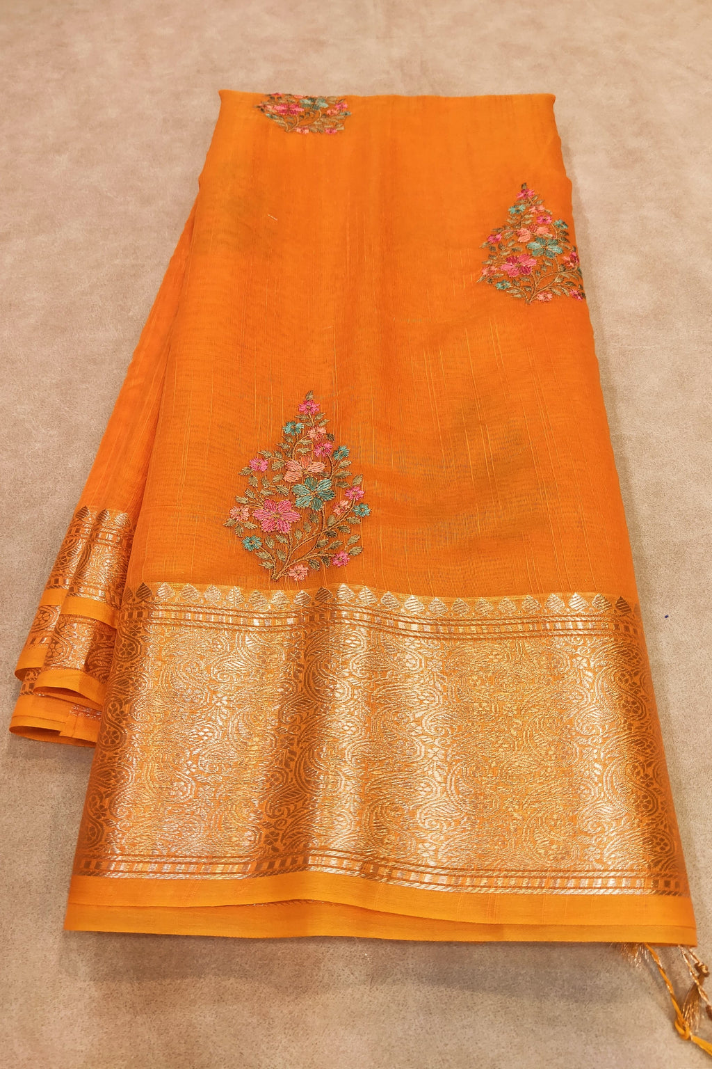 Orange fabric with floral embroidery and gold border on a beige background