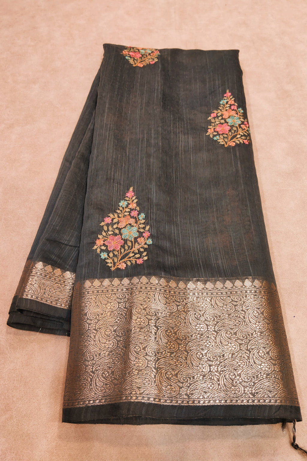 Black saree with floral embroidery on a beige background