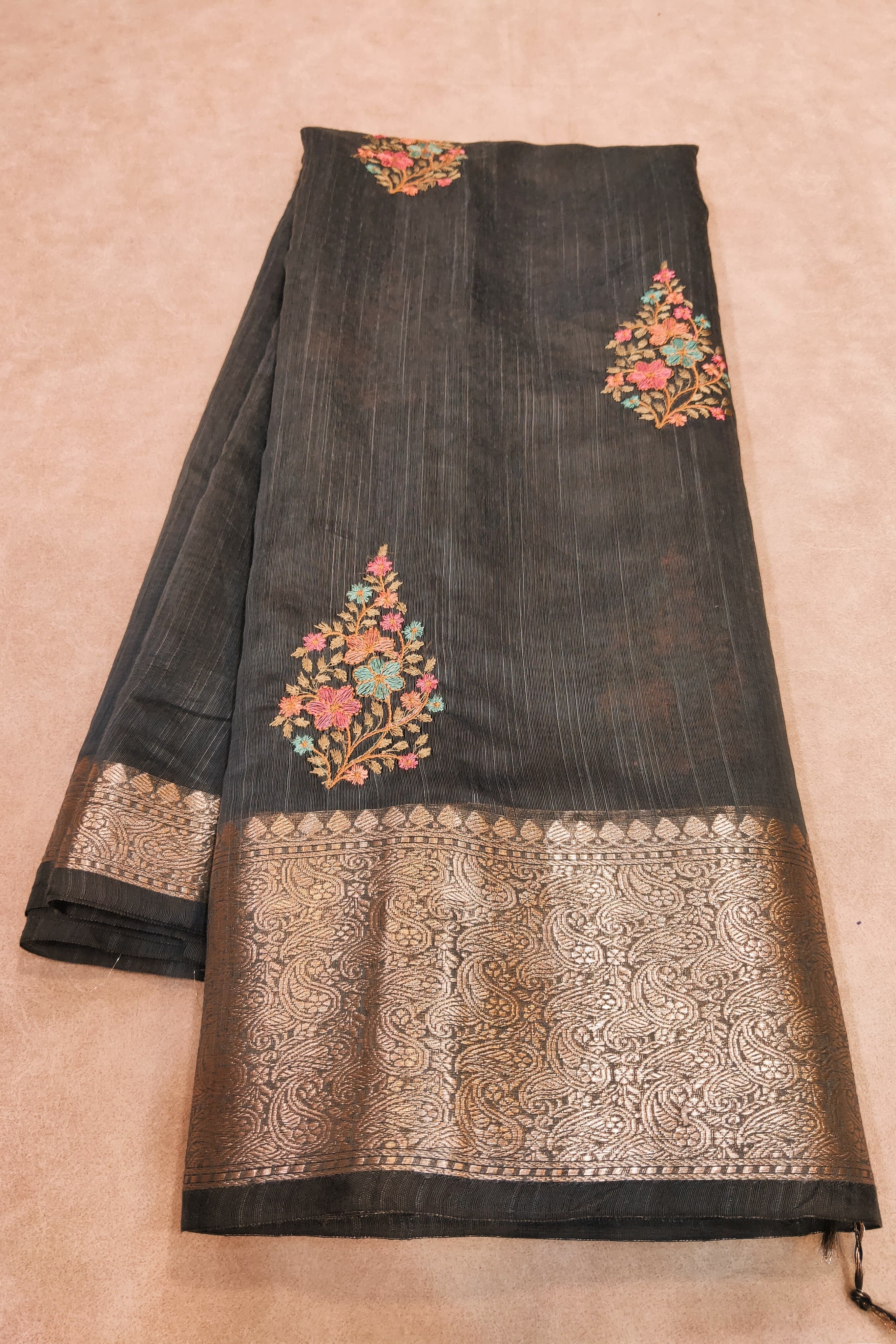 Black saree with floral embroidery on a beige background