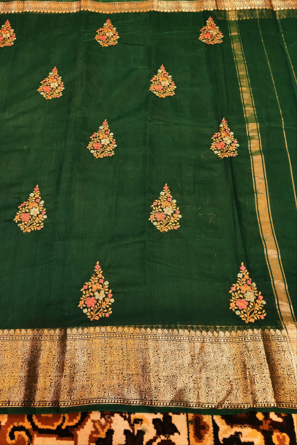 Green saree with gold and pink floral patterns on a patterned fabric background