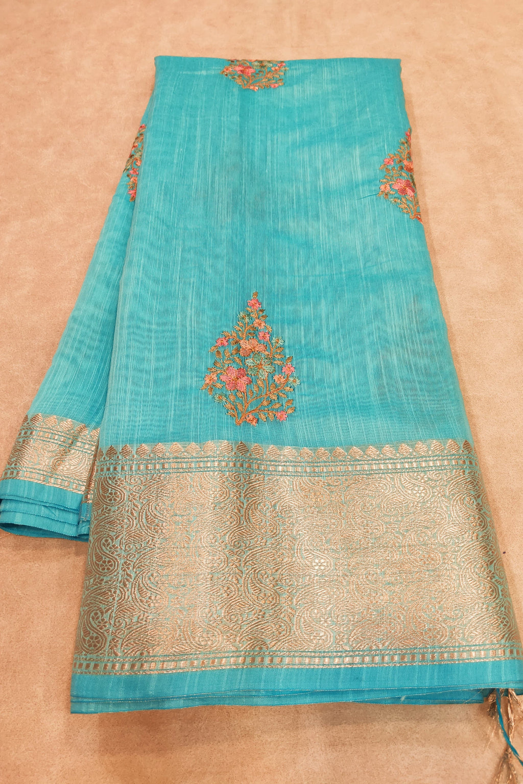 Turquoise saree with gold border and floral patterns on a beige background