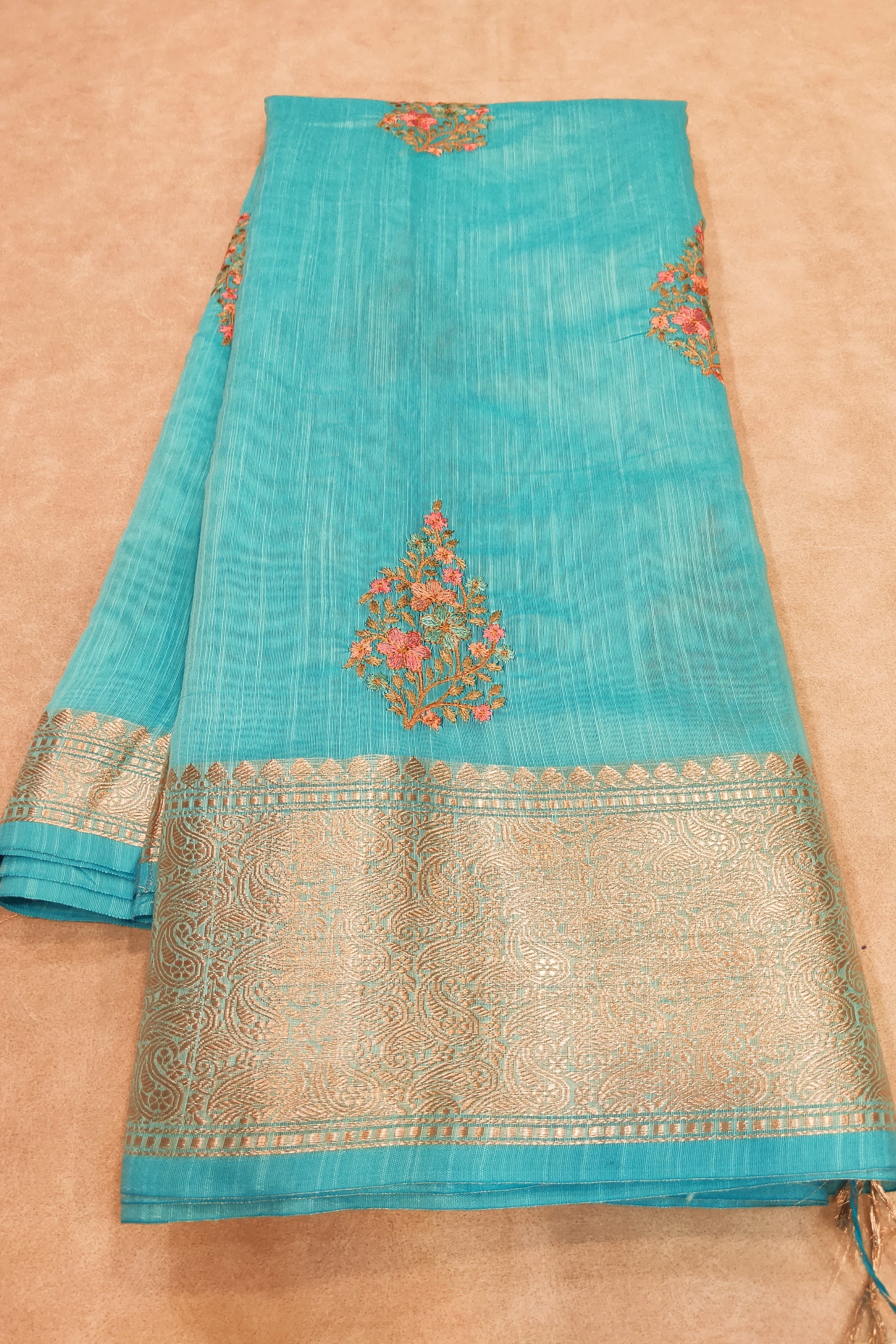 Turquoise saree with gold border and floral patterns on a beige background