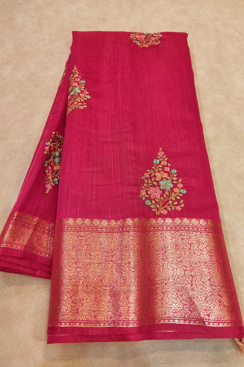 Red saree with gold and floral embroidery on a beige background