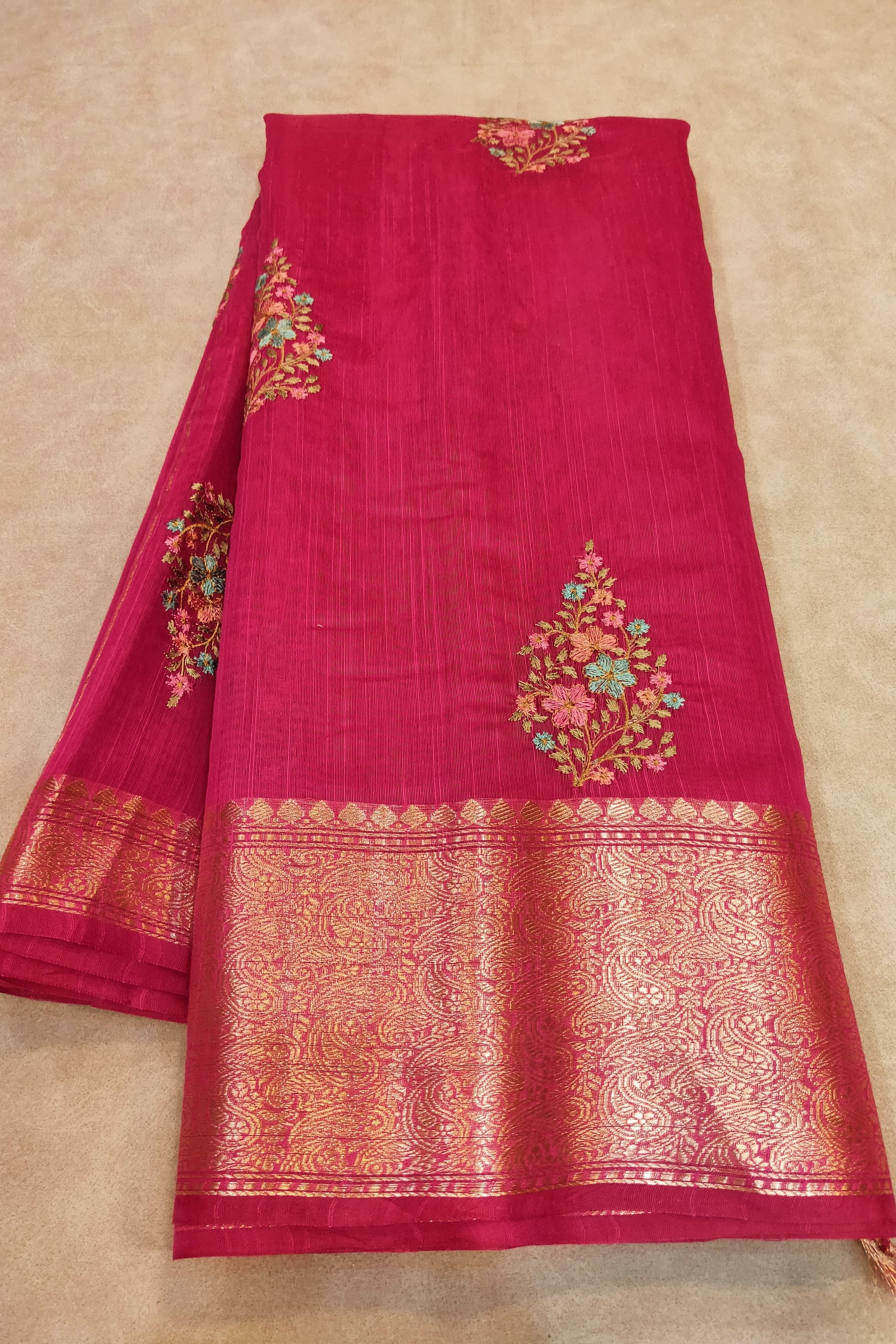 Red saree with gold and floral embroidery on a beige background