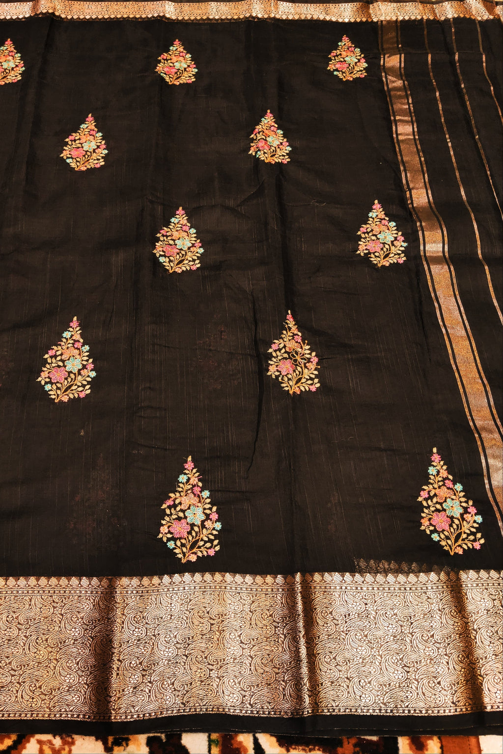 Black saree with floral embroidery and a brown border on a wooden surface