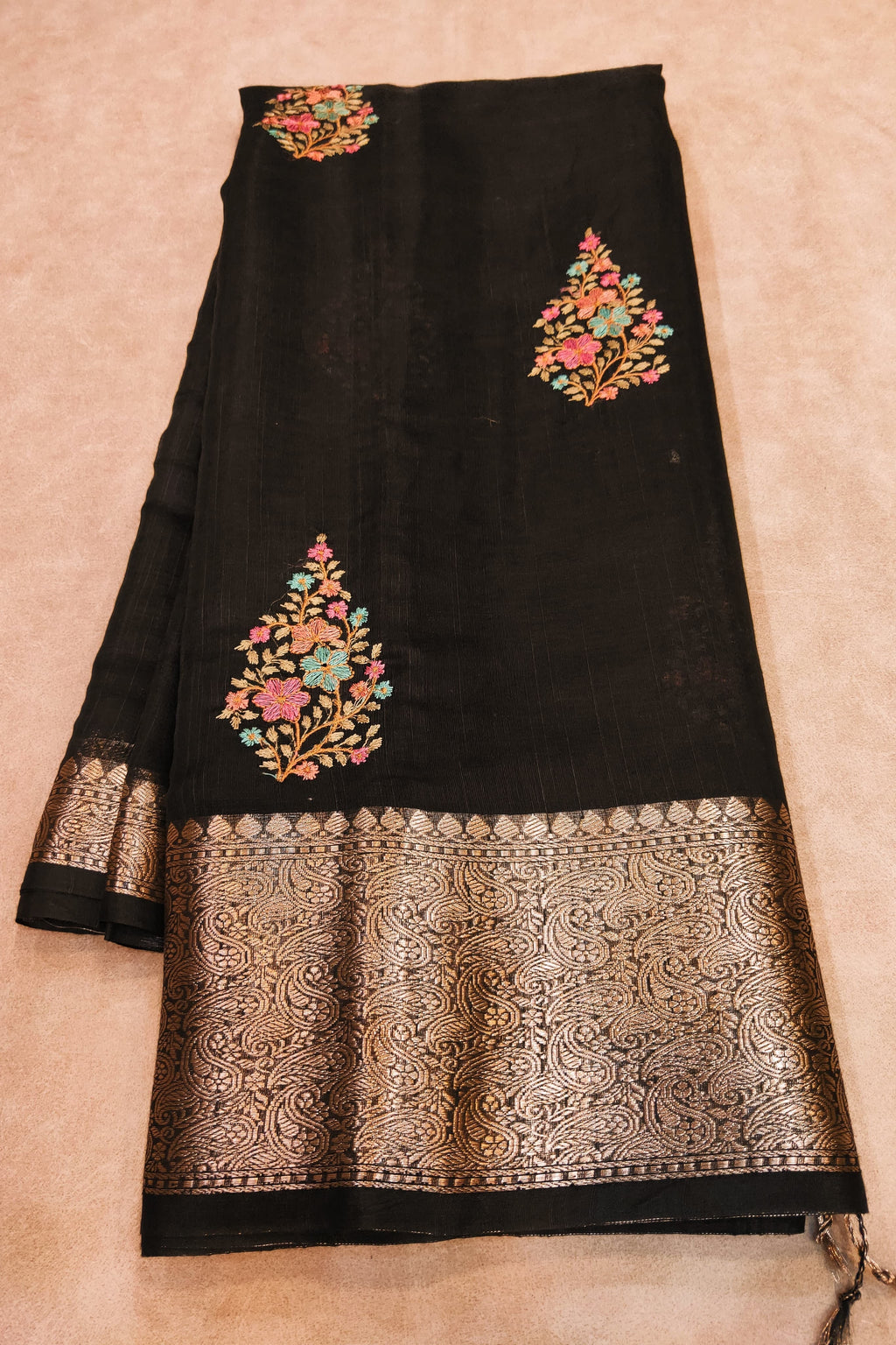 Black fabric with floral embroidery and gold border on a beige background