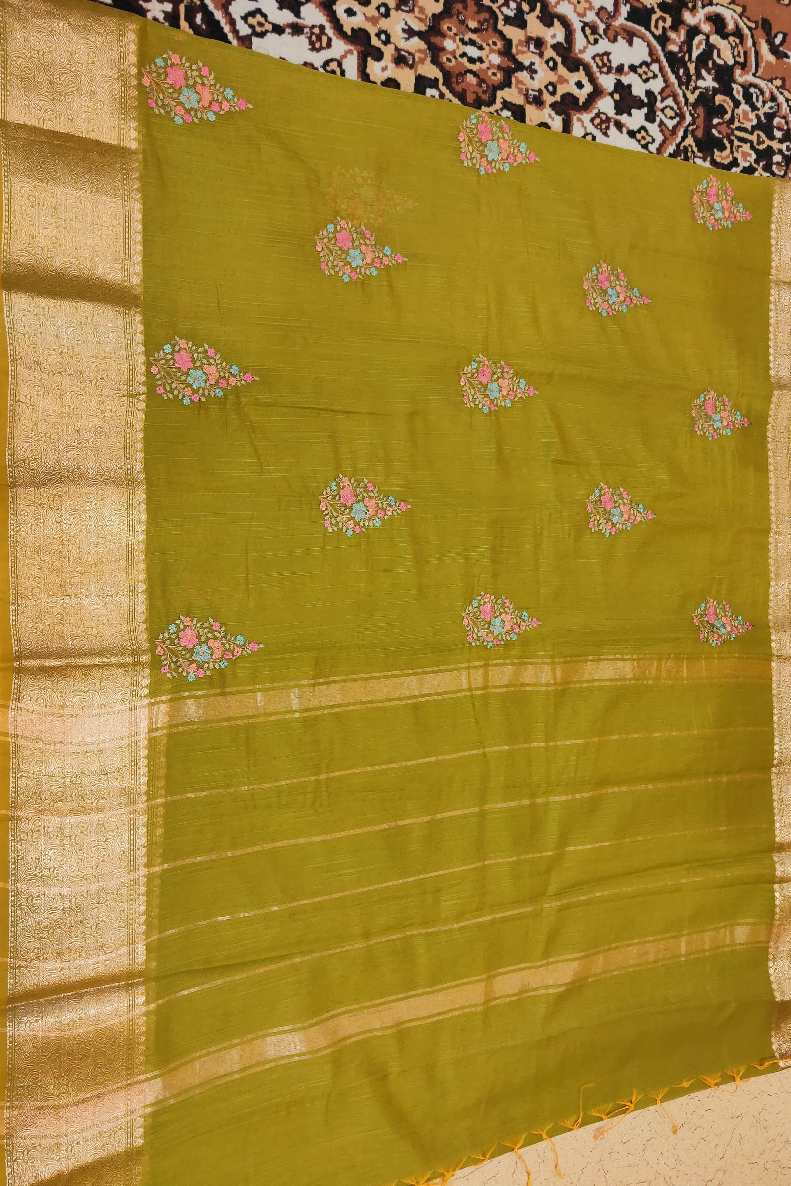 Green saree with floral patterns on a patterned fabric background
