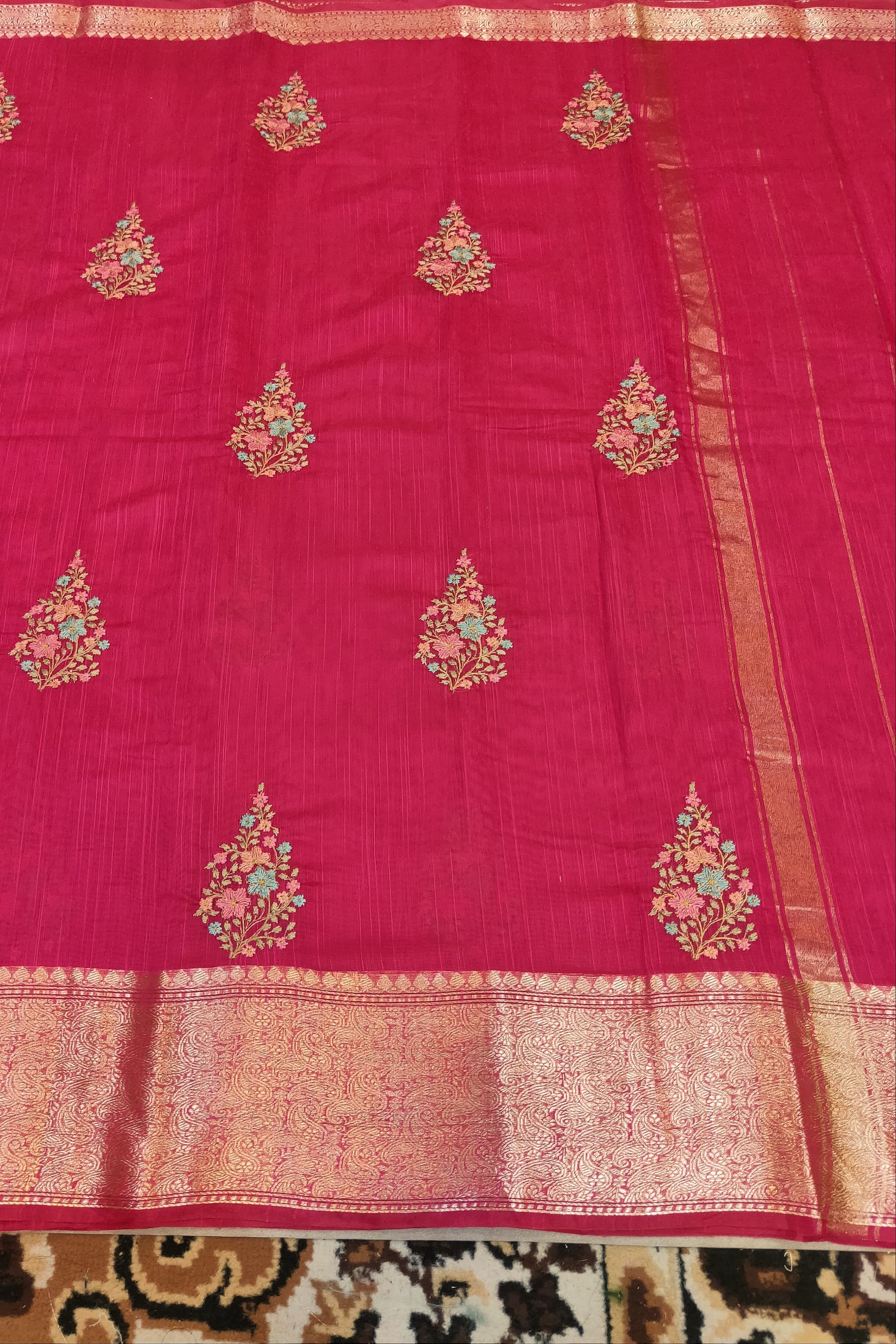 Pink saree with gold and green embroidery on a patterned fabric background
