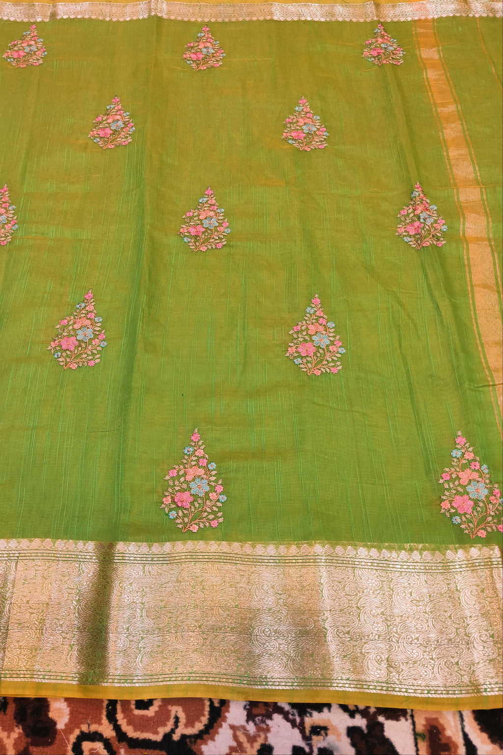 Green saree with floral patterns on a patterned fabric background