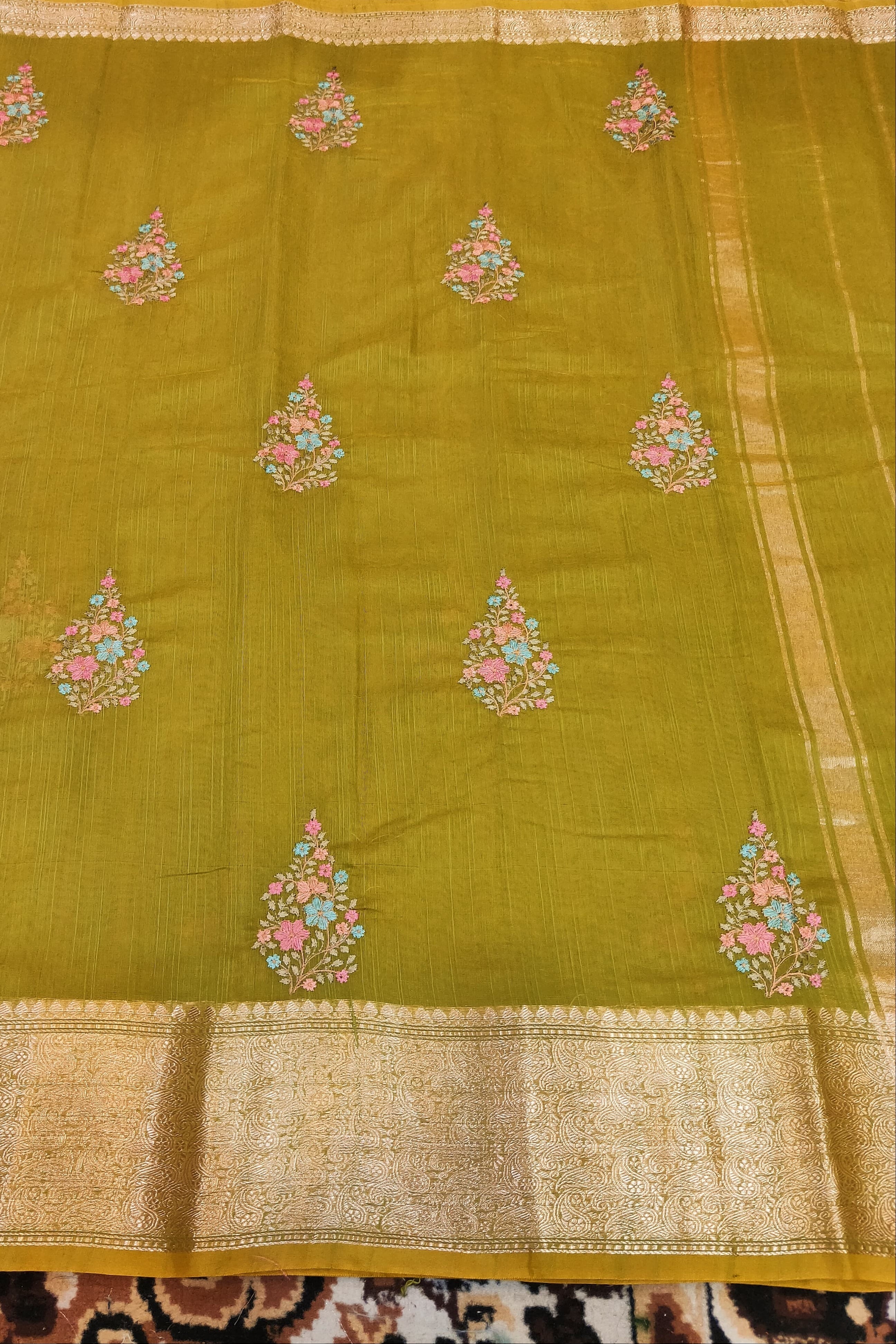 Green saree with floral patterns on a patterned fabric background