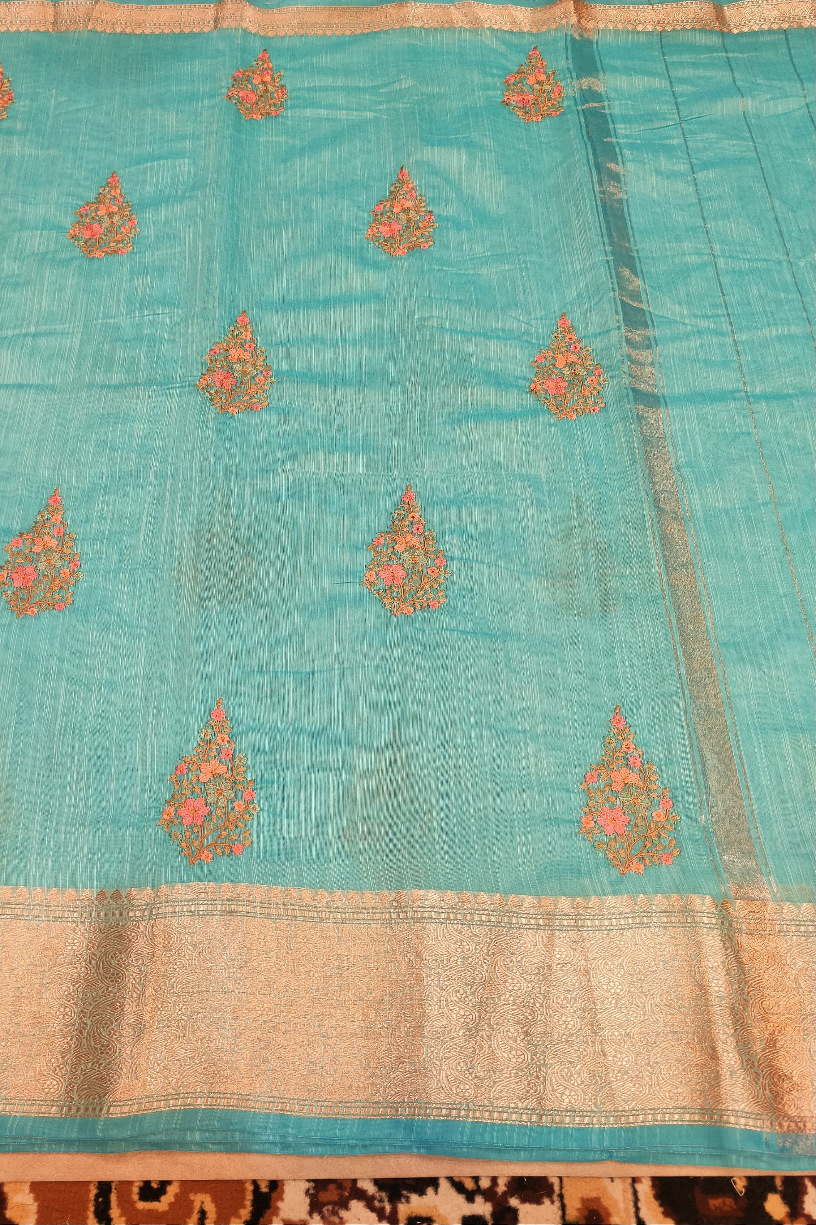 Light blue fabric with gold and pink embroidery on a wooden surface