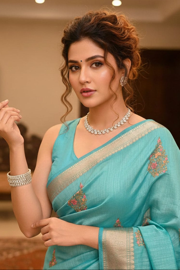 Woman wearing a turquoise saree with floral patterns indoors