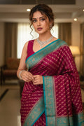 Woman wearing a traditional maroon saree with a blue border indoors.