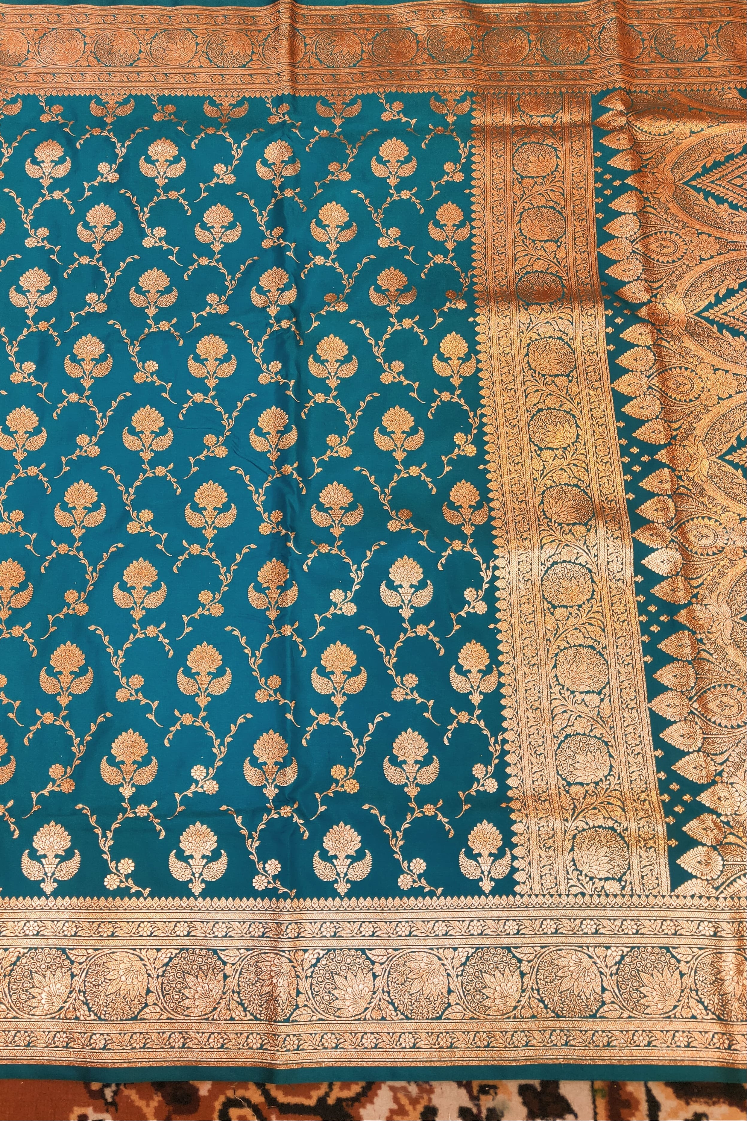Teal fabric with gold floral patterns on a textured background