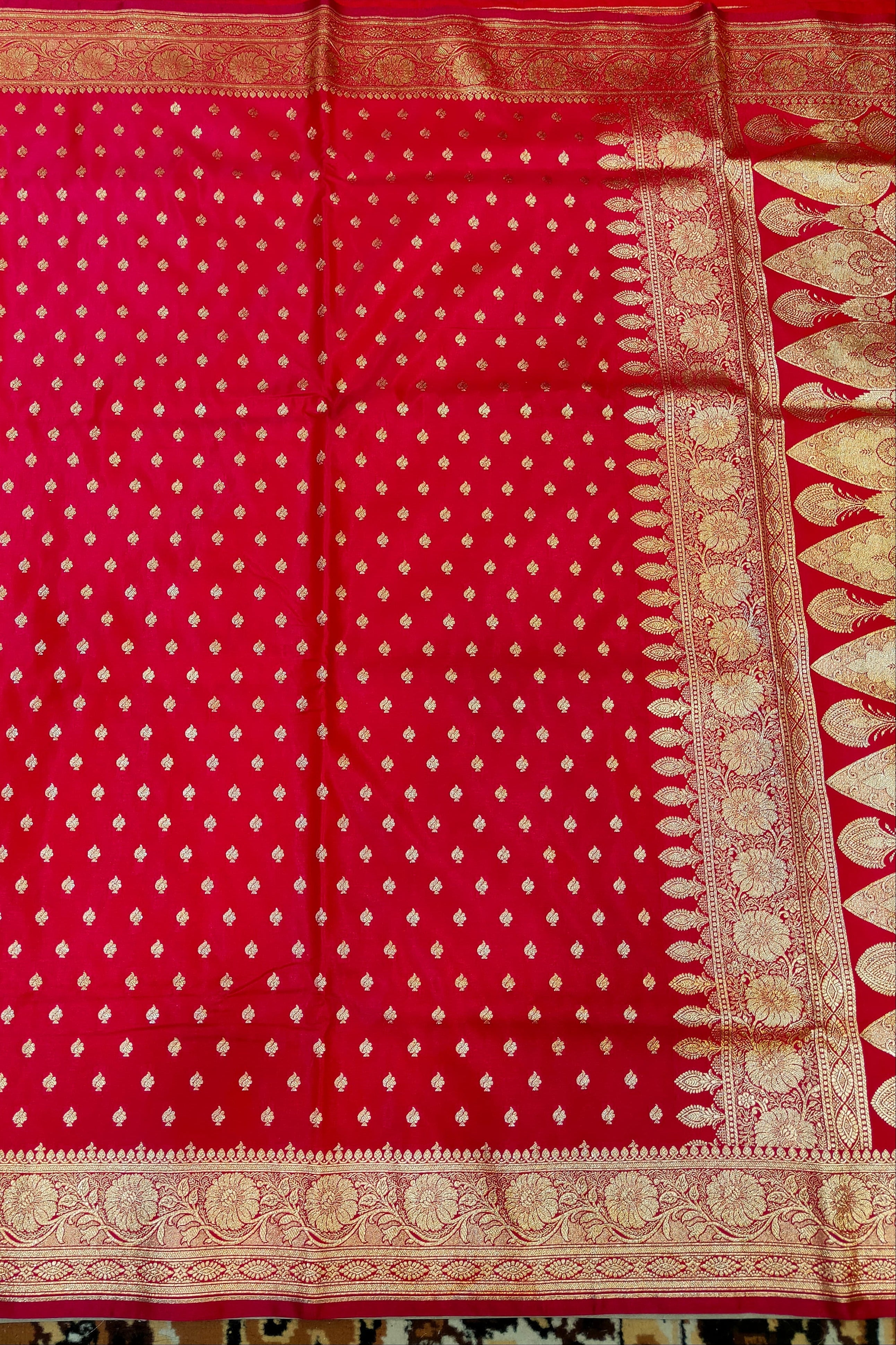 Red fabric with white patterns and gold border on a patterned background