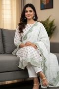 Woman in a white and green traditional outfit sitting on a gray couch.