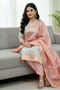 Woman in a pink saree sitting on a gray couch in a bright room.