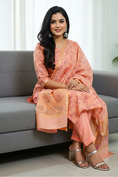 Woman in a peach saree sitting on a gray couch in a well-lit room.