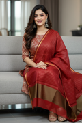 Woman in a red and gold saree sitting on a gray couch.