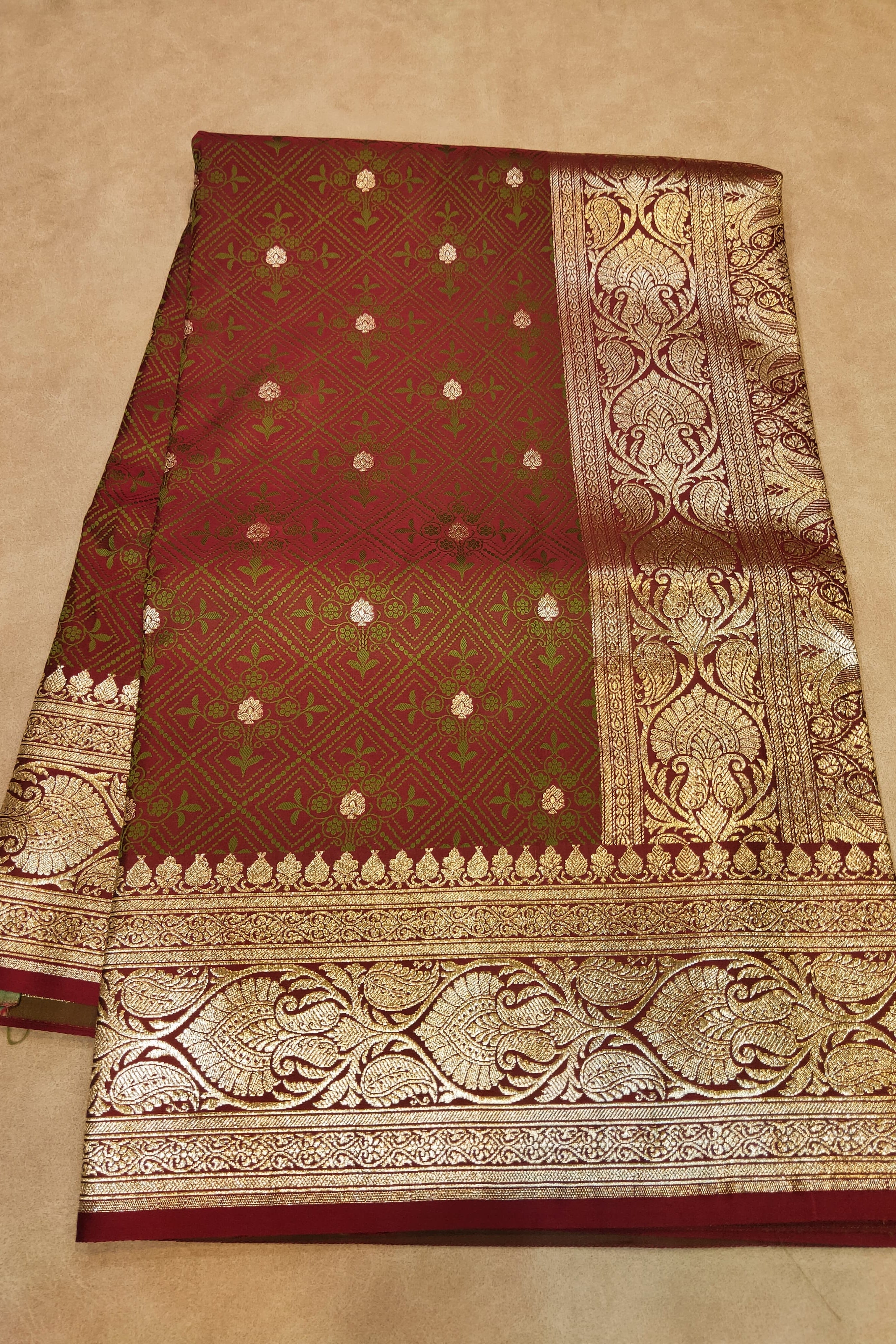 Brown saree with gold and green patterns on a beige background
