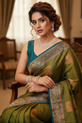 Woman in a green saree with a blue blouse sitting on a chair.