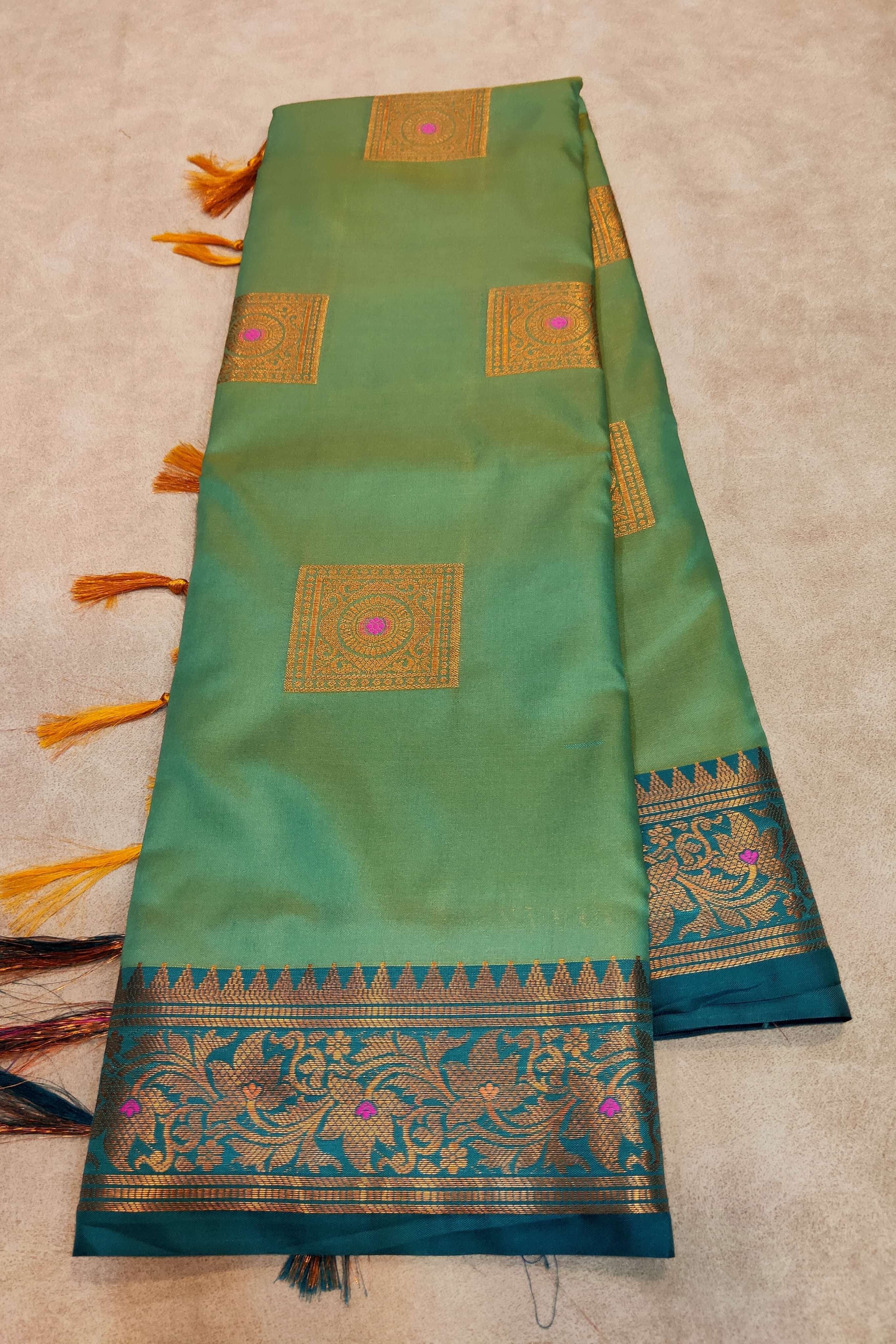 Green saree with gold and blue patterns on a beige background