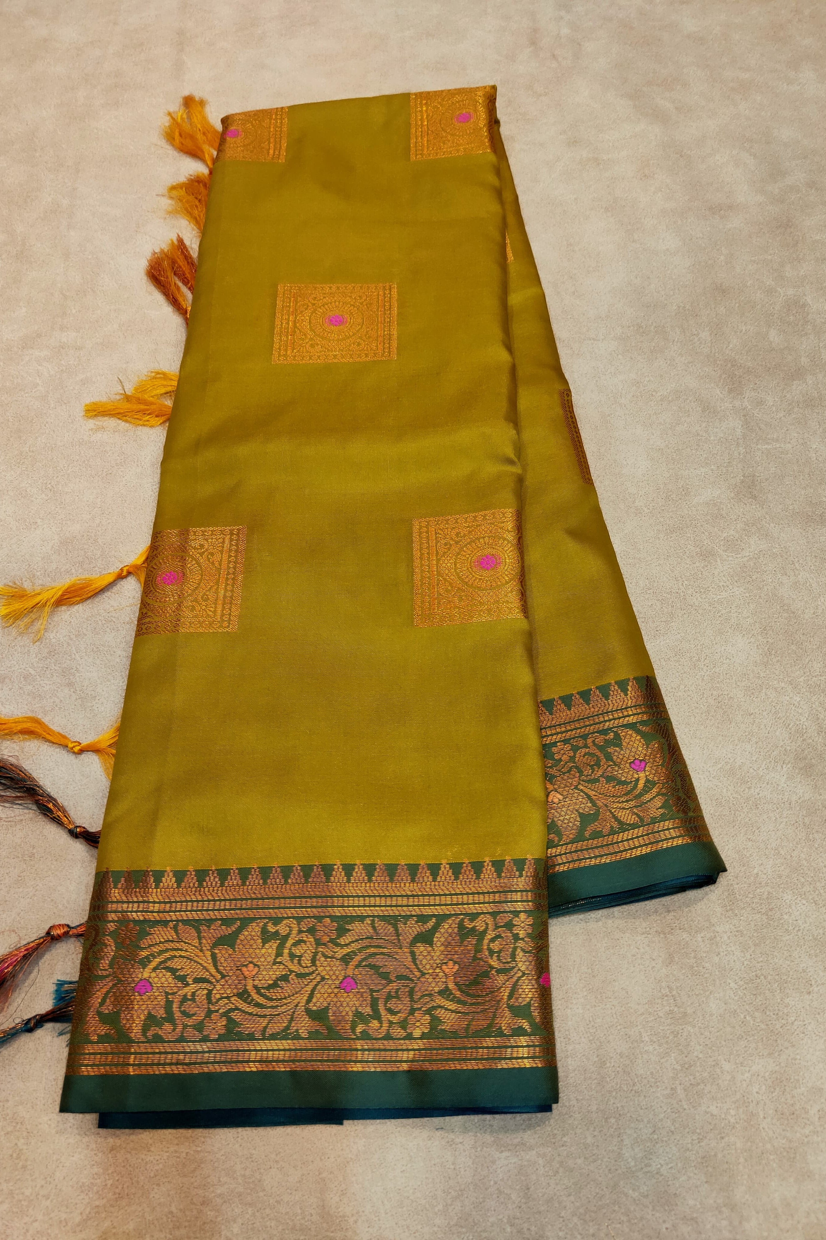 Green saree with gold border and tassels on a beige background