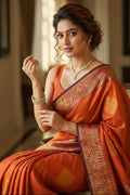 Woman in an orange saree with gold patterns indoors