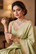 Woman in a light green saree with jewelry, sitting indoors.